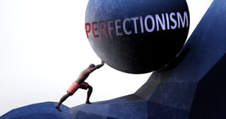 Illustration of a person pushing a huge boulder labeled PERFECTIONISM up a steep rocky slope.